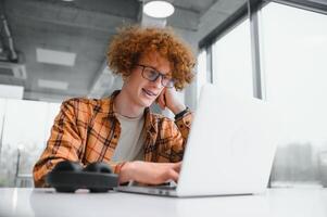 Image of amazing young man sitting in cafe while using laptop computer. photo