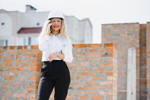 construcción ingeniero. niña con construcción documentación. un mujer en un blanco difícil sombrero en contra el techo de un edificio. construcción de un nuevo casa foto