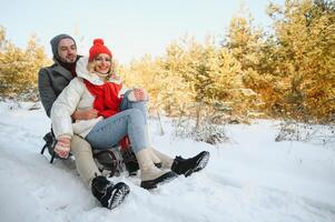 A side view of a happy couple having fun while sliding downhill together over snowy slope using a sled photo