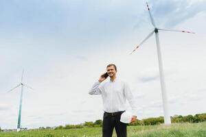 Windmill engineer talking on the phone on windmill and sky background. A man in a helmet supervises the operation of the electric windmills. photo