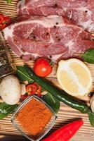 Raw pork meat with spices and vegetables on wooden table. photo