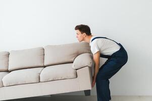 Loader moves sofa, couch. worker in overalls lifts up sofa, white background. Delivery service concept. Courier delivers furniture in case of move out, relocation. photo