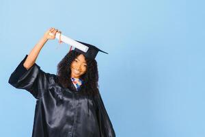 African-American beautiful woman in a black robe and hat, on a blue isolated background smiles. photo