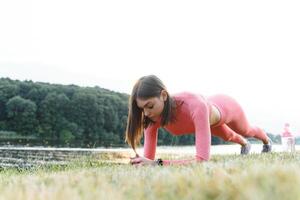 Young caucasian woman doing active training exercise on a yoga mat near the river in summer. Concept of healthy lifestyle photo