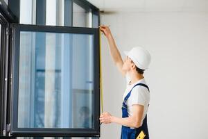 Workman in overalls installing or adjusting plastic windows in the living room at home photo