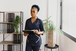 Portrait of beautiful smiling female african american doctor standing in medical office. Health care concept, medical insurance, copy space photo