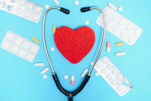 Close-up of a heart and a stethoscope on a blue background, top view. Global health care concept. caring for heart health. treatment with tablets and ampoules. photo