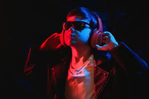 Studio shot in dark studio with neon light. Portrait of a stylish boy with headphones photo