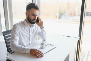 Portrait of a young realtor in the office at the table. Real estate sales concept. photo