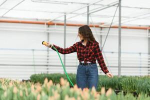 hermosa joven sonriente chica, trabajador con flores en invernadero. concepto trabajo en el invernadero, flores foto