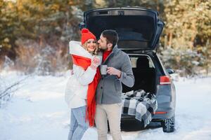 Cute Couple Having Winter Forest Picnic Drinking Tea from Tea Take Away Cup. Nature Picnic. Love Story Date at Car. photo