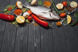 Raw sea fish dorado with lemon, pepper, tomatoes and various spices. On a black rustic background. photo
