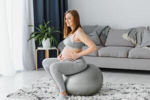 Young pregnant woman exercising yoga with fit ball at home photo