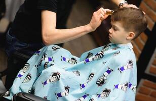 lado ver de linda pequeño chico consiguiendo Corte de pelo por peluquero a el peluquería. foto