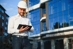 Engineer next to building cranes. Concept - large construction project. Architect directs the construction process. Drawings and tablet in the hands. photo