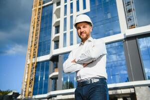 Engineer next to building cranes. Concept - large construction project. Architect directs the construction process. Drawings and tablet in the hands. photo