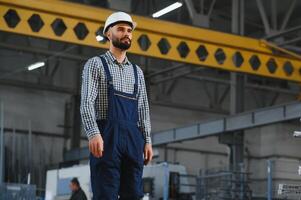 Portrait of Professional Heavy Industry Engineer Worker Wearing Safety Uniform, Hard Hat Smiling. In the Background Unfocused Large Industrial Factory. photo