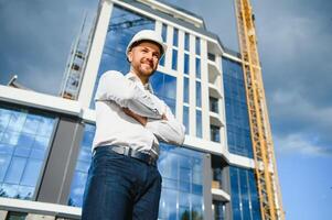 Engineer next to building cranes. Concept - large construction project. Architect directs the construction process. Drawings and tablet in the hands. photo
