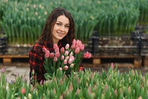 Beautiful young smiling girl, worker with flowers in greenhouse. Concept work in the greenhouse, flowers, tulips, box with flowers. Copy space. photo