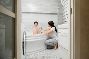 Mother washing little son in bathroom photo