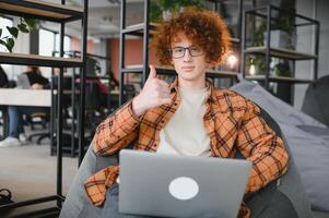 Young happy male freelancer in casual clothes sitting in cafe with laptop and using mobile phone. photo