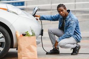 africano americano hombre cargando su eléctrico coche. foto