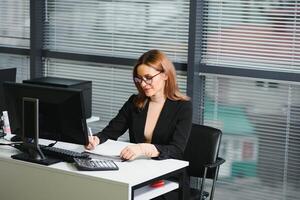 joven mujer de negocios sentado a lugar de trabajo y leyendo papel en oficina foto