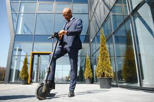 Handsome african 30s man wearing coat smiling while riding electric scooter outdoors photo