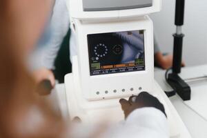 moderno médico equipo. cerca arriba de oftalmólogo utilizando auto refractómetro mientras examinando niño ojos. foto