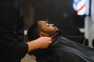 negro hombre en el peluquería. linda negro hombre hace un Corte de pelo en el africano salón. pelo estilo. Corte de pelo para adultos foto