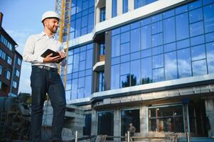 Engineer next to building cranes. Concept - large construction project. Architect directs the construction process. Drawings and tablet in the hands. photo