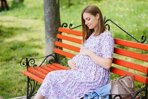 The young pregnant woman has a rest on a bench in park photo