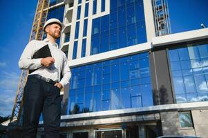 Engineer next to building cranes. Concept - large construction project. Architect directs the construction process. Drawings and tablet in the hands. photo