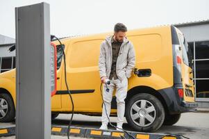 Man Holding Power Charging Cable For Electric Car In Outdoor Car Park. And he s going to connect the car to the charging station in the parking lot near the shopping center photo