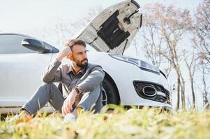 Sad driver holding his head having engine problem standing near broken car on the road. Car breakdown concept photo
