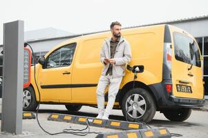 Man Holding Power Charging Cable For Electric Car In Outdoor Car Park. And he s going to connect the car to the charging station in the parking lot near the shopping center photo