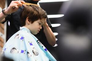 lado ver de linda pequeño chico consiguiendo Corte de pelo por peluquero a el peluquería. foto