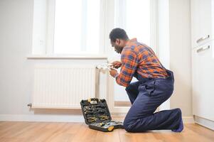 Repair heating radiator close-up. African man repairing radiator with wrench. Removing air from the radiator photo