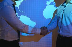 Handshake with map of the world in background. two businessmen on the background of the world map shake hands, the concept of international relations photo