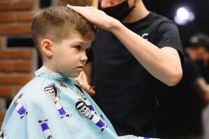 un pequeño linda chico se sienta en un peluquería a el estilista, un alumno es consiguiendo pelo cortar en un belleza salón, un niño a un barberías, un corto de los hombres Corte de pelo foto