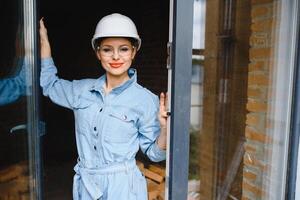 Construction concept. Pretty female builder in overalls and helmet working on construction site. photo