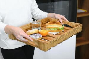 Young woman holding tray with breakfast food at home photo