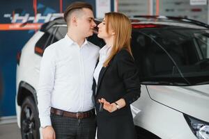 Visiting car dealership. Beautiful couple is holding a key of their new car and smiling, girl is kissing her husband in cheek. photo