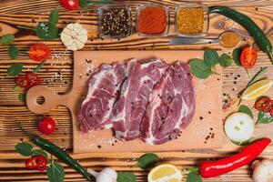 Raw pork meat with spices and vegetables on wooden table. photo