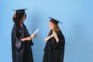 Two girls are posing for take photo in black gowns and hold diploma certificate. They are graduates and hold diploma certificate. They are happy and in good mood.