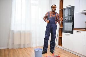 profesional limpiador en azul uniforme Lavado piso y limpiando polvo desde el mueble en el vivo habitación de el departamento. limpieza Servicio concepto foto