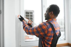 obrero en mono instalando o ajustando el plastico ventanas en el vivo habitación a hogar foto