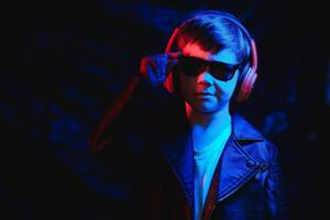 Studio shot in dark studio with neon light. Portrait of a stylish boy with headphones photo