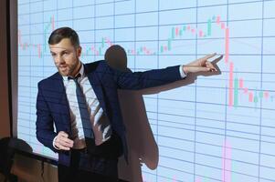 Man is standing near projector and showing graphs and business graphs. photo