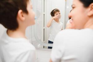 Beautiful mother and happy son brushing teeth near mirror in bathroom photo